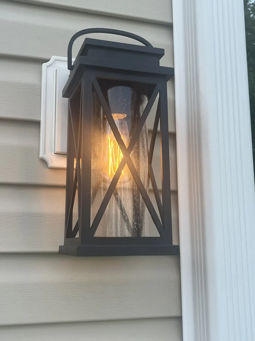 Black lantern sconce glowing on a home's siding after installation