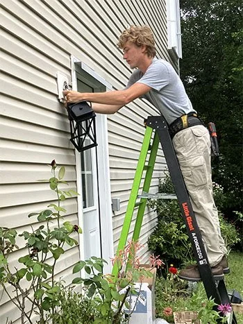 Light of the World electrician installing an exterior light fixture from a ladder